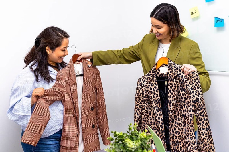 Two women engage in an image consulting session, discussing fashion choices. One holds a plaid blazer, while the other presents a leopard print coat, showcasing style variety