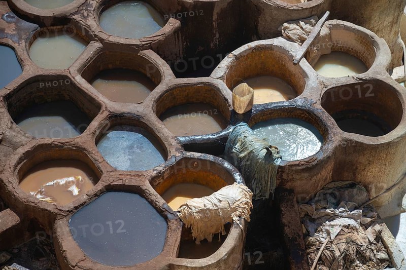 Aerial view of traditional leather tanning pits filled with vibrant dye baths in warm sunlight in Fez, Morocco. The ancient artistry showcases a stunning array of colors and textures