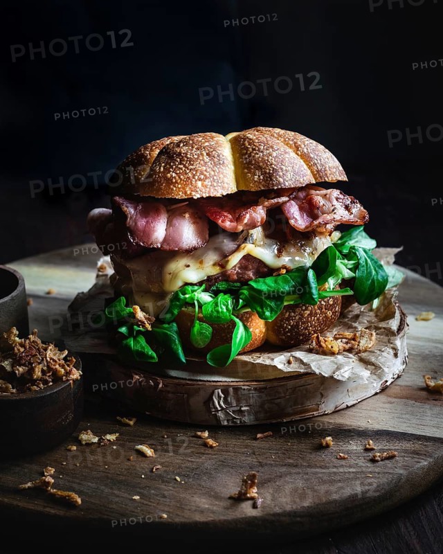 A delicious gourmet burger featuring crispy bacon, fresh lettuce, and melted cheese, perfectly layered between soft pumpkin bread. Served on a rustic wooden board with crispy onion garnish
