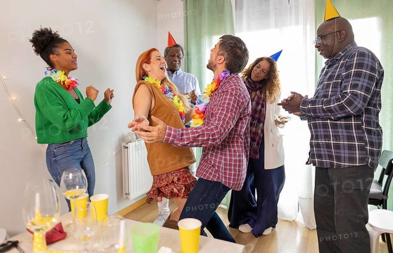 A lively birthday party with friends laughing and dancing, wearing colorful hats and leis. Glasses and festive decorations enhance the joyful atmosphere
