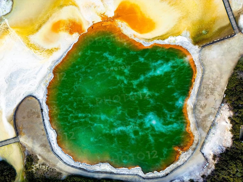 A breathtaking aerial view of Champagne Pool in Wai-O-Tapu geothermal park, New Zealand, showcasing vibrant hues of orange, yellow, and green surrounded by natural formations