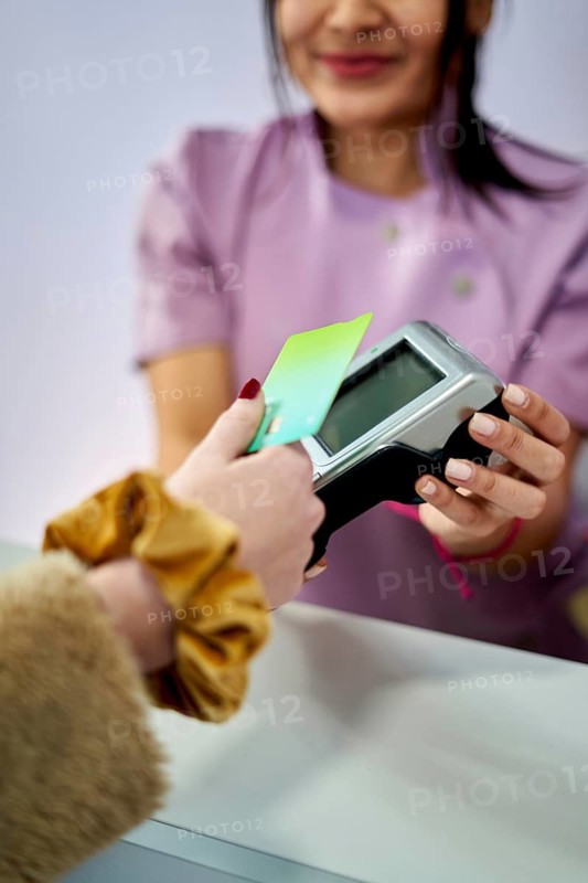 A customer hands a payment card to a salon staff member at a beauty salon. The staff member smiles as they assist with the transaction in a welcoming atmosphere