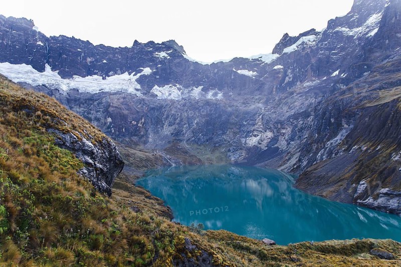 A breathtaking glacial crater lake with turquoise waters, surrounded by rugged cliffs and snow-capped peaks at El Altar volcano, Ecuador, reflecting the dramatic Andean landscape