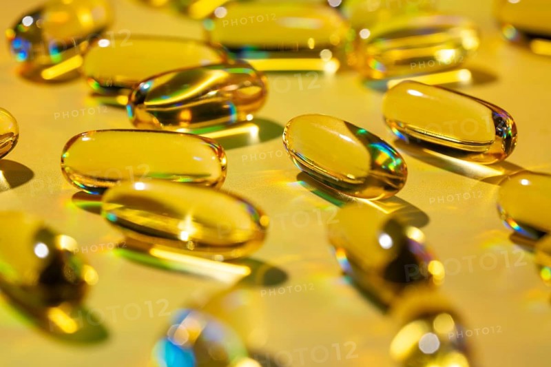 Close-up of golden softgel capsules containing essential vitamins, reflecting light. Ideal for promoting health and wellness as a convenient dietary supplement option