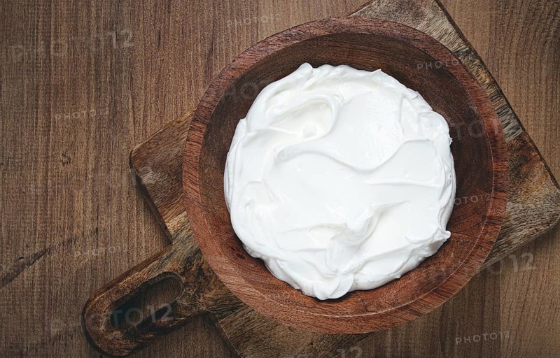 Sour cream in a wooden bowl, on a wooden table, top view, close-up, no people
