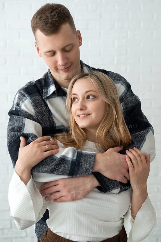 A young man and woman share a tender embrace in a brightly lit home, conveying warmth and closeness. Their affectionate pose and joyful expressions exemplify a loving relationship