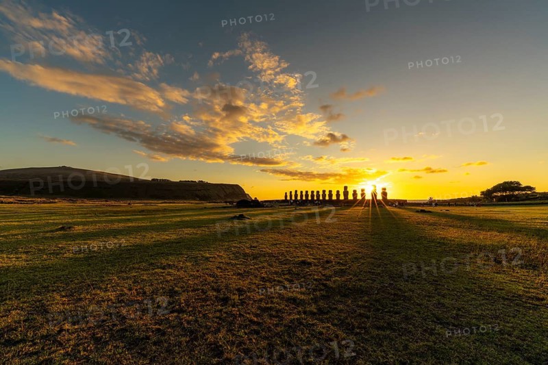 Moai statues of Ahu Tongariki as silhouettes at sunrise, grassy area in the foreground, cloudy sky, Easter Island, Chile