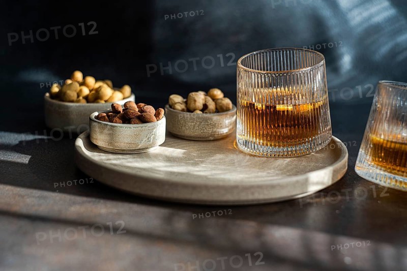 An elegantly plated spiced cognac cocktail, complete with a cinnamon and star anise, paired with assorted nuts including almonds, peanuts, and hazelnuts, captured in a moody lit setting