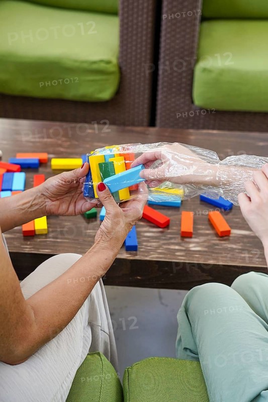 A mother and daughter are engaged in a colorful board game, fostering connection and fun. Bright wooden blocks are scattered, symbolizing family togetherness and play