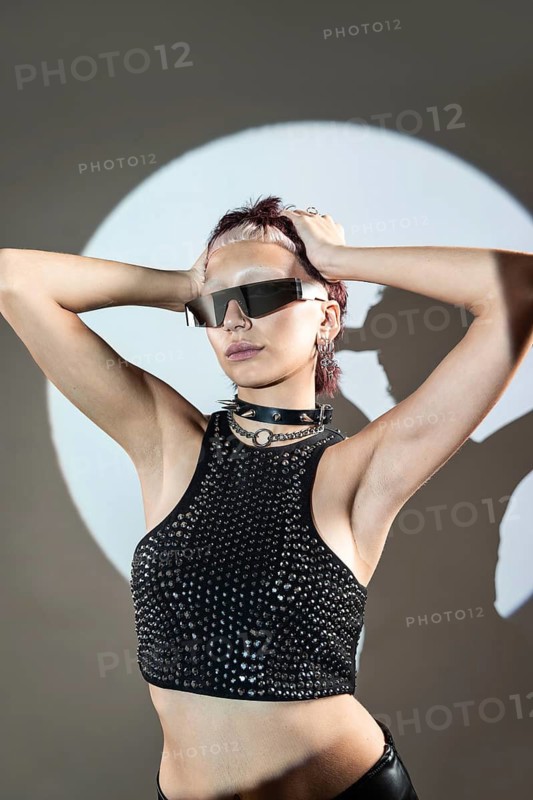 A striking cyberpunk woman model in futuristic fashion wears edgy sunglasses and a studded top, embodying a bold, innovative style against a modern, minimalist backdrop