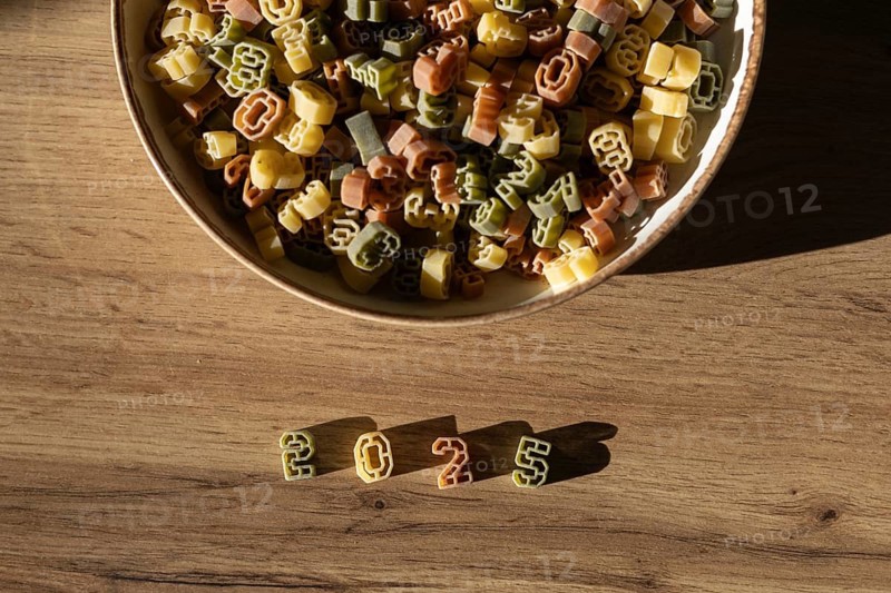 Top view of colorful number shaped pasta in a bowl and the number 2025 clearly arranged on a wooden surface, representing the new year