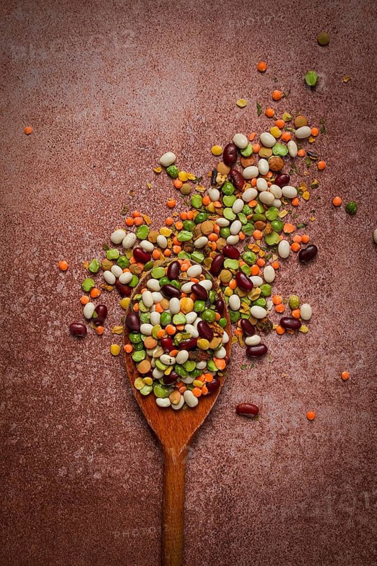 Wooden spoon, with an assortment of legumes, beans, peas, top view, on a brown background