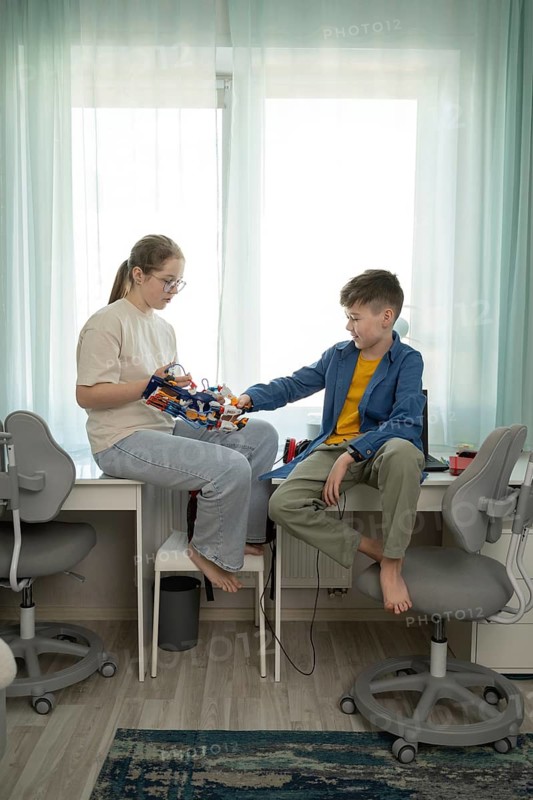 A girl and boy share a bonding moment with an educational toy while sitting on a desk. The serene room, natural light, and modern furnishings create a cozy atmosphere
