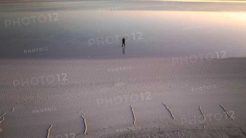 A solitary figure stands on the expansive salt flats of Salinas Grandes, Salta, Argentina, reflecting the serene evening sky. The tranquil scene captures the essence of solitude and natural beauty