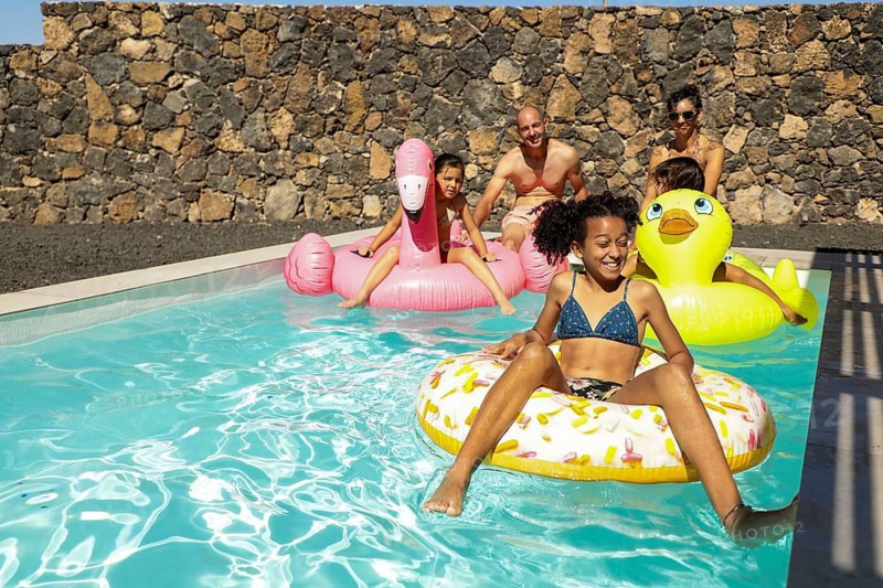 A joyful family relaxing in a sparkling pool, surrounded by colorful inflatable floats. Bright afternoon sunlight casts playful shadows on the water
