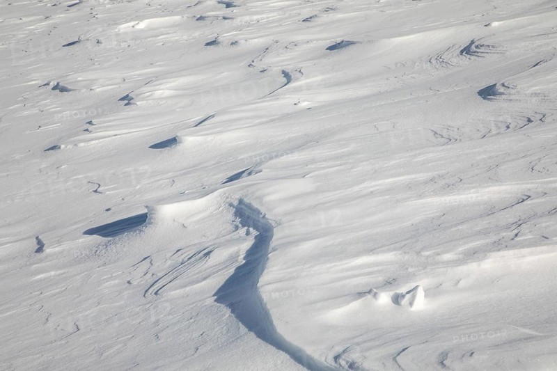 An expansive view of a textured snow-covered field with various shapes and formations carved by wind and weather