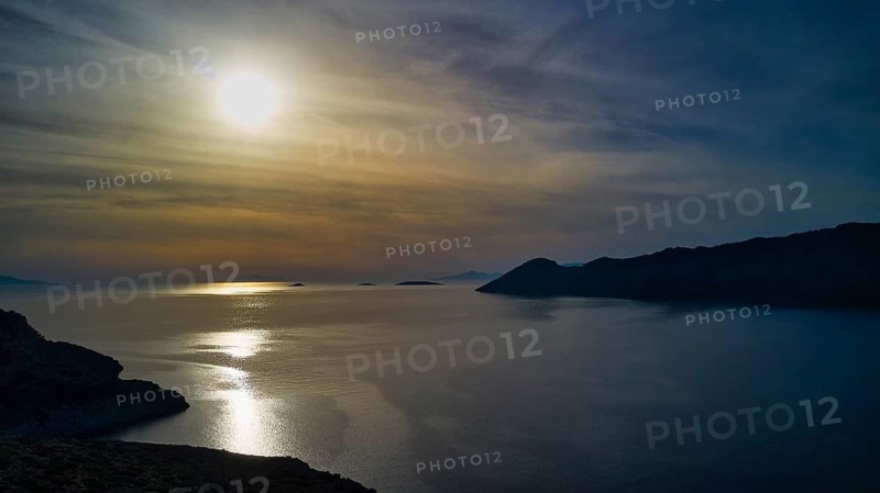 Drone shot, Romantic sunset over calm sea with islands on the horizon, Holy Week, Bay of Panormitis, Panormitis Monastery, Symi, Dodecanese, Greek Islands, Greece