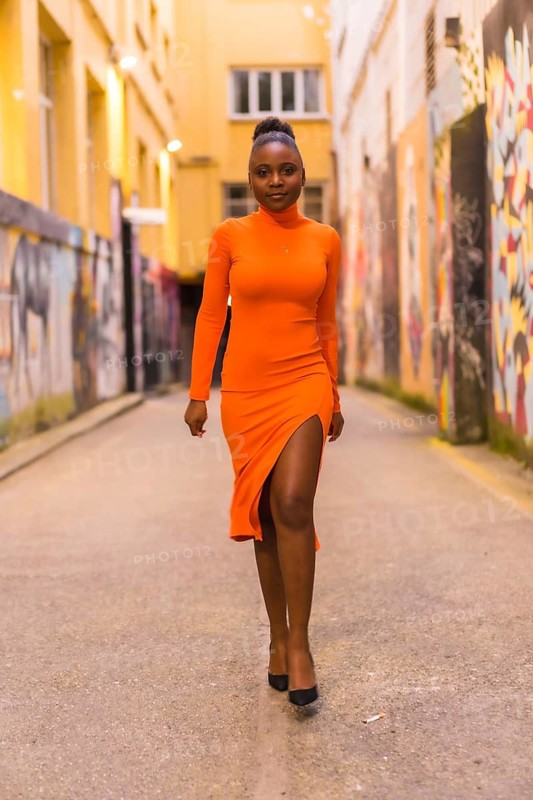 Fashionable urban style with a black African girl in an orange dress and black heels on a city street. Walking in the photoshoot