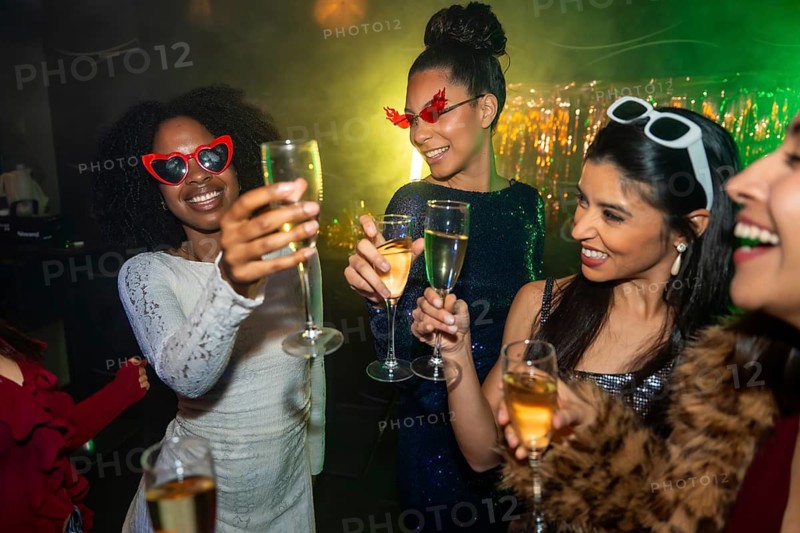 Diverse group of young women enjoying a night out, celebrating and toasting with champagne during a festive party with vibrant lights and sparkling decorations in a club setting
