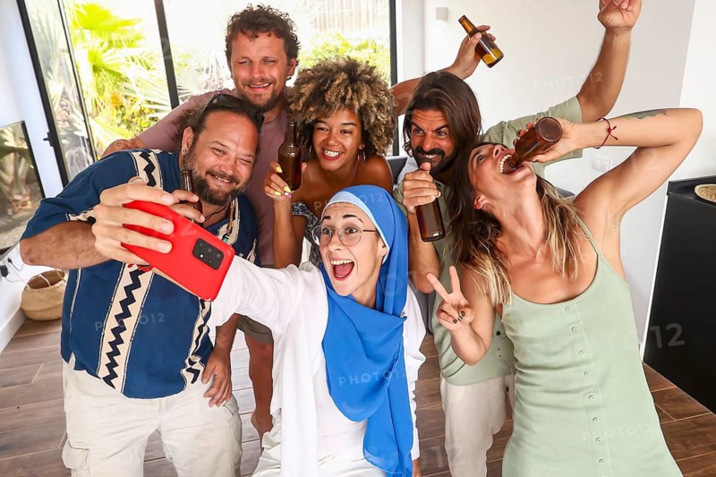 A diverse group of friends captures the joy of a lively indoor party with drinks and laughter They pose for a fun selfie, showcasing camaraderie and celebration
