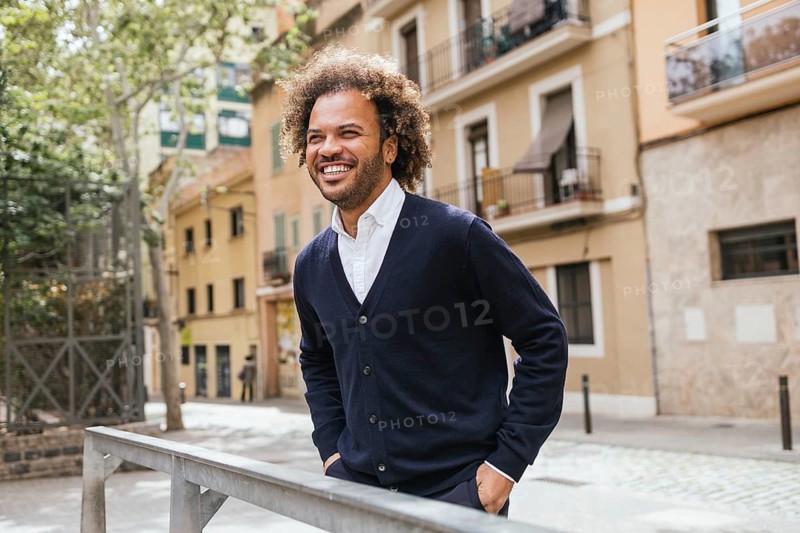 A cheerful man is seen enjoying a break, smiling as he strolls through a picturesque street in Barcelona, surrounded by beautiful architecture and vibrant urban scenery