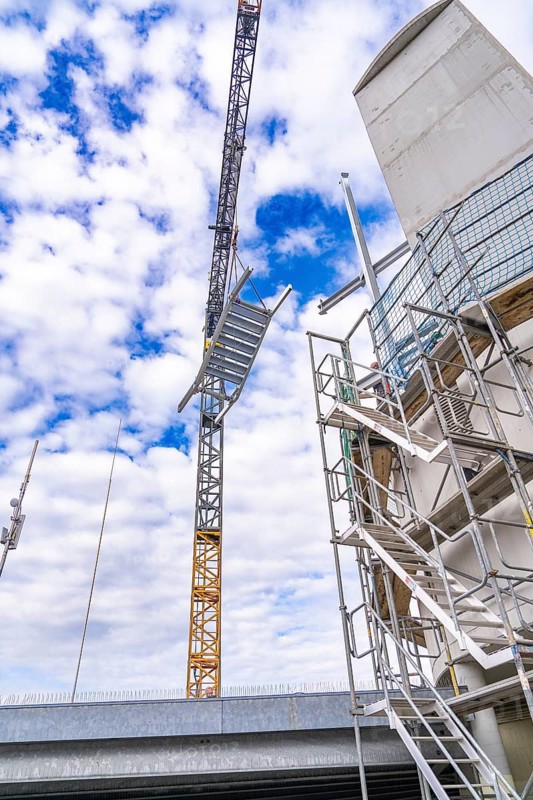Crane lifts a structure next to a scaffolding under a cloudy sky, showing modern architecture, staircase extension to the new tower of the Calw railway station on the new track of the Hermann Hessebahn, Calw, Black Forest, Germany