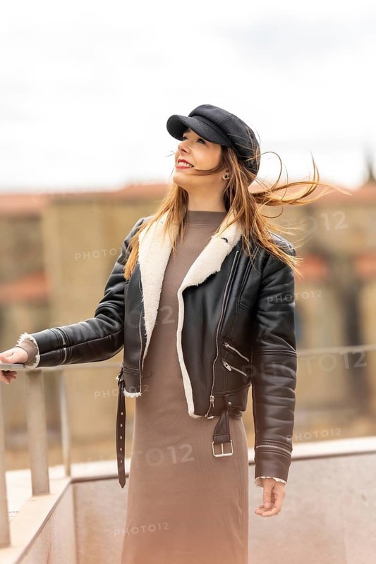 Fashionable woman wearing a black cap and leather jacket, enjoying the urban landscape with wind blowing her hair