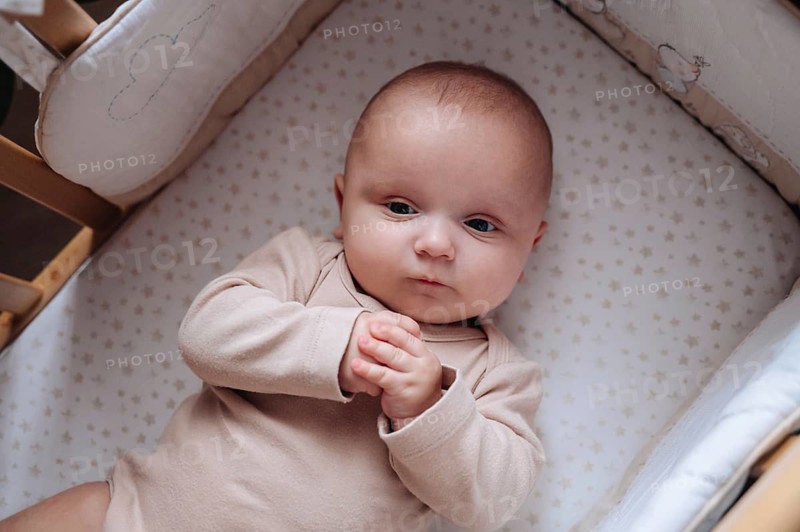 A baby boy lies comfortably in a crib, gazing thoughtfully. He wears a soft onesie, surrounded by a cozy blanket. The peaceful scene captures innocence and tranquility