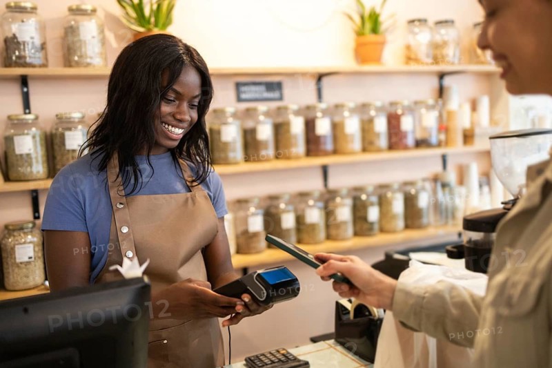 A smiling cashier assists a customer using a smartphone for payment at an organic supermarket, highlighting the convenience of modern digital transactions in a sustainable environment