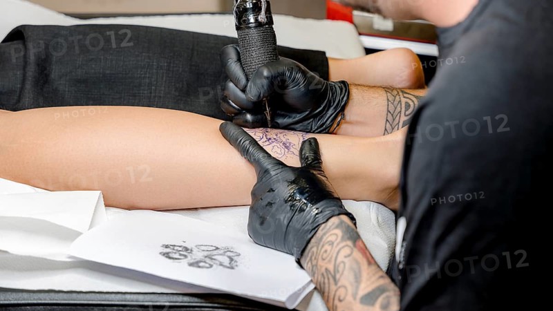 Professional tattoo artist carefully works on creating a detailed ink design on a client's leg, showcasing precision and artistry in modern tattoo techniques