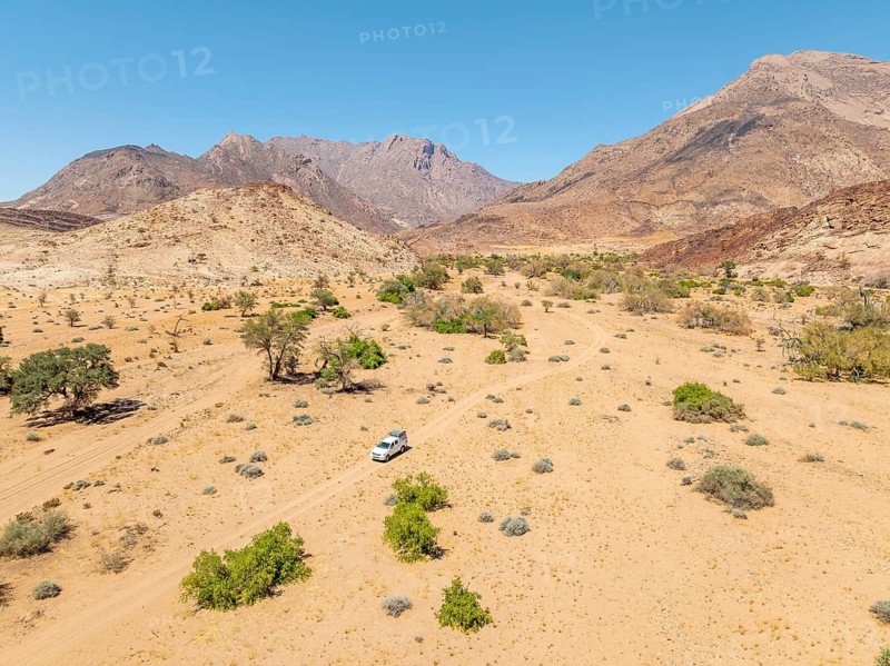 Aerial view of off-road car driving in dry riverbed and desert landscape on the Ugab River, behind Brandberg, Erongo, Damaraland, Namibia
