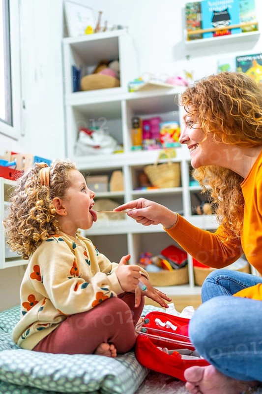 Vertical photo of a caucasian mother examining the tongue of her daughter playing nurses