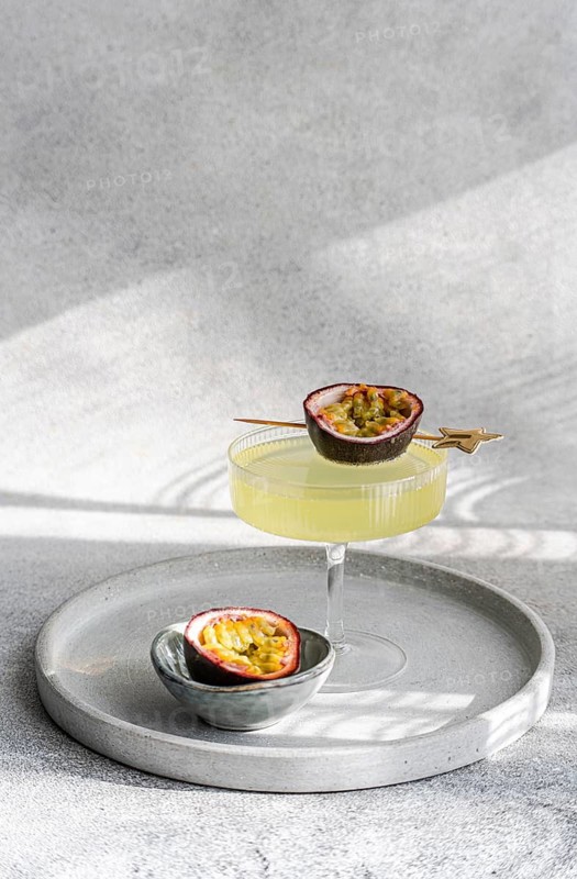 A stylish cocktail made with tonic, gin, and passion fruit juice served in an elegant glass. A halved passion fruit adds a decorative and exotic touch atop a silver tray under soft lighting