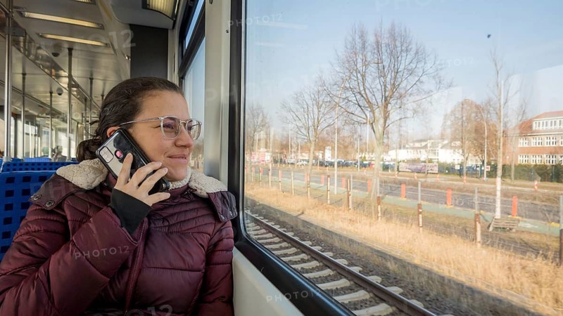 A woman in glasses enjoys a train ride, chatting on her smartphone. She gazes out the window, surrounded by the serene winter landscape visible outside
