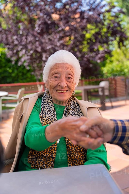 Hands of two elderly people in the garden of a nursing home or retirement holding hands in a moment of affection