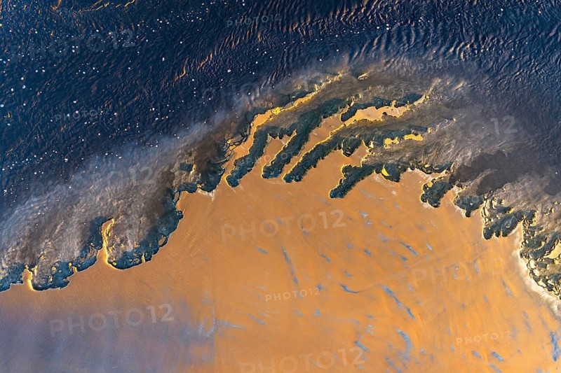 An aerial shot captures a vivid, abstract landscape blending orange and blue hues in a dynamic, flowing pattern