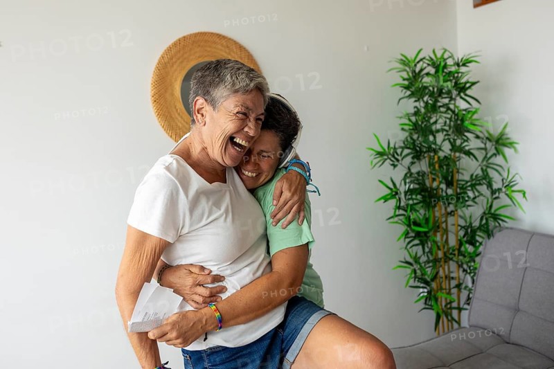 Joyful lesbian couple embracing and laughing as they prepare for their upcoming summer holidays, expressing happiness and love in a cozy home setting