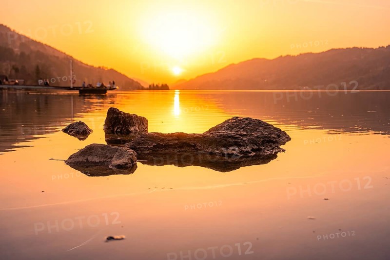 Sunset over a lake with rocks and landscape rolling gently into the mountains, Großer Alpsee, Immenstadt im Allgäu, Bavaria, Germany