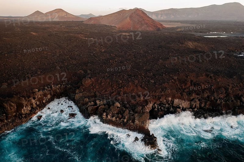 Captivating aerial shot showcasing the rugged coastline and volcanic terrain of Los Hervideros, Lanzarote, with waves crashing along the shore at sunset