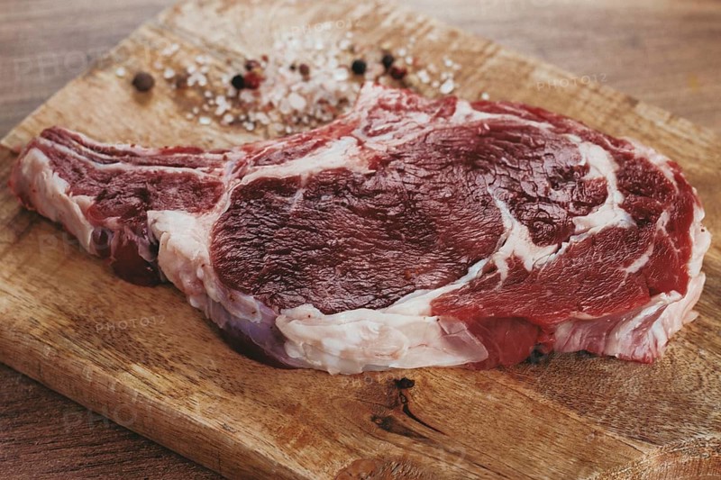 Raw rib eye steak, cowboy steak, on a wooden chopping board, top view, no people