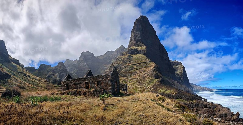Stone ruins of old houses made of volcanic stone against a spectacular mountain backdrop with thick clouds and blue sky, hiking, lost place, abandoned village of Formiguinhas, Marinha da Cruzinha Natural Park, Santo Antao, Cabo Verde, Cape Verde, Cape Verde