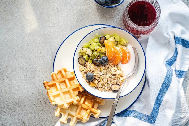 A delicious breakfast scene featuring granola with yogurt, kiwi, blueberries, orange slices, and waffles on a plate. A vibrant and nutritious start to the day