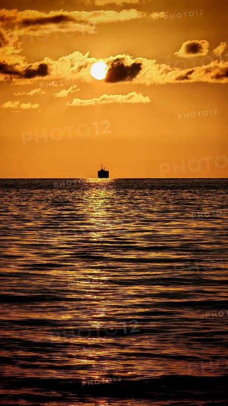 Single ship in golden sunlight reflecting romantically on the calm sea under a clear sky, Batumi, Georgia