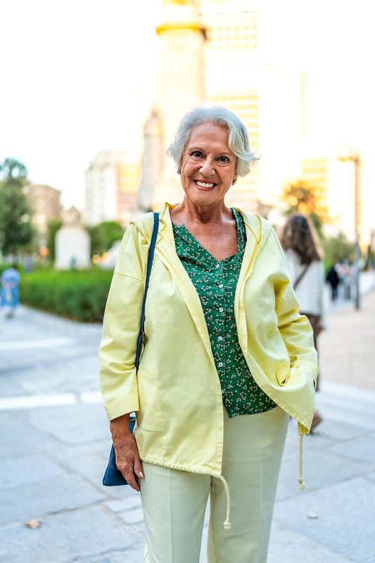Vertical portrait of a modern senior woman standing in the city street smiling at camera