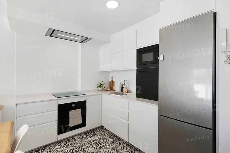 Minimalist kitchen featuring white cabinetry, patterned flooring, stainless steel appliances, and modern lighting in the city center. Elegant and functional space ideal for cooking