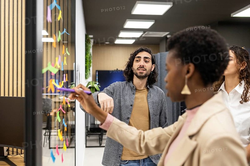 A team discusses creative ideas while using colorful sticky notes on a glass board in a modern office. They engage in collaborative brainstorming to foster innovation