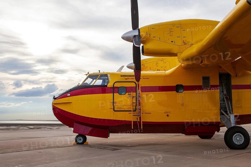 A vibrant yellow Bombardier aircraft on the runway at Torrejon Air Base, Spain. The plane is ready for an airshow, set against a cloudy sky backdrop. Ideal for aviation enthusiasts