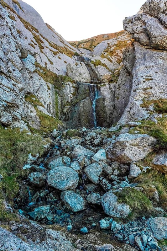 Stunning waterfall cascades down rugged rocks in mount txindoki, surrounded by lush greenery and dramatic cliffs in the basque country