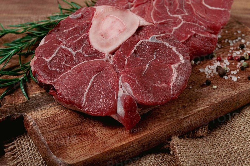 Knuckle on the bone, raw meat for ossobuco, on a wooden chopping board, with a sprig of rosemary, and spices, top view, no people