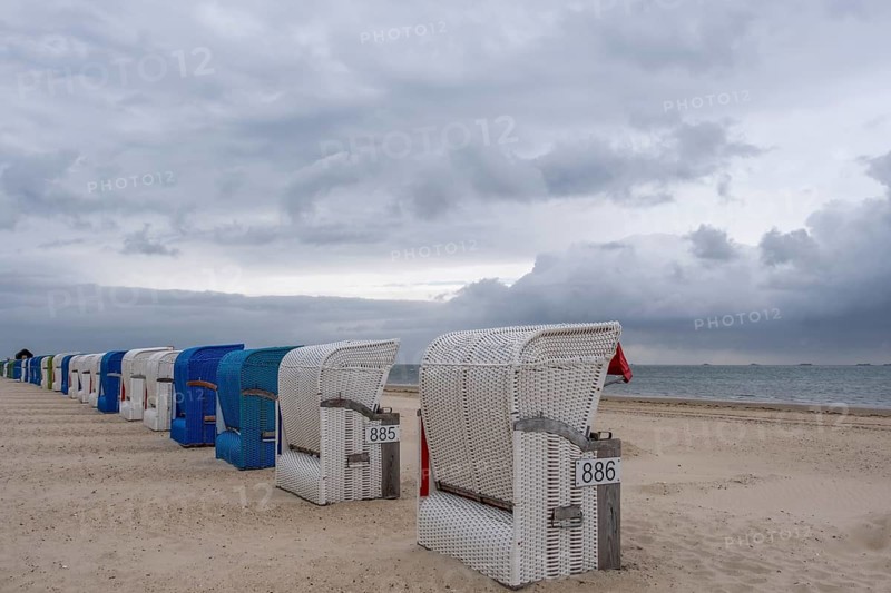 Row of white and blue beach chairs on the beach under a cloudy grey sky, Föhr, Nordfriesland, Schleswig-Holstein, Germany